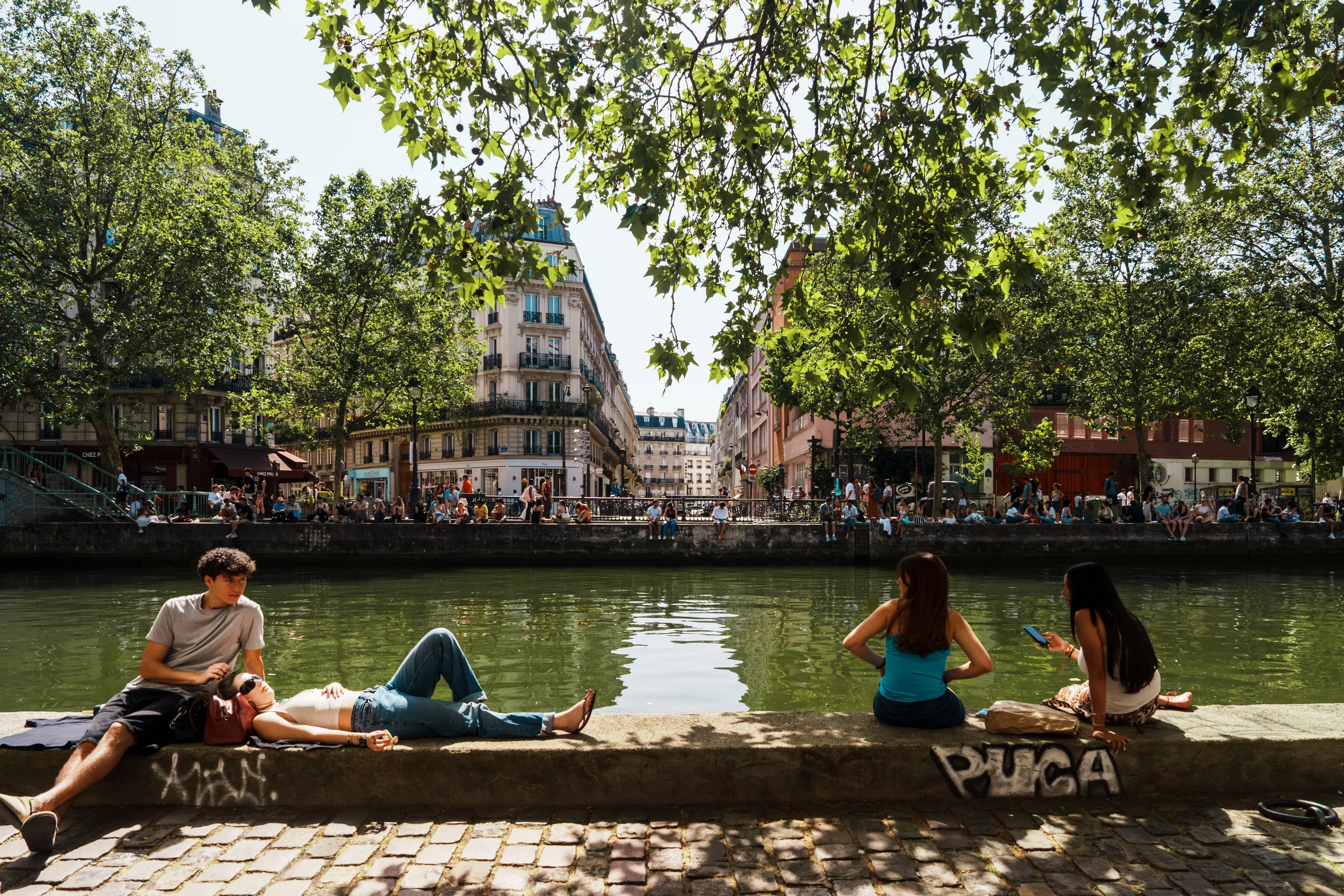 People relaxing beside a tree-lined canal in France